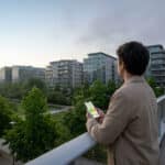 Un homme regarde un smartphone affichant un graphique de qualité de l'air sur une passerelle face à des immeubles.