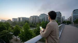 Un homme regarde un smartphone affichant un graphique de qualité de l'air sur une passerelle face à des immeubles.