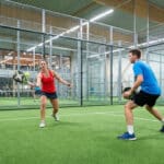 Un homme et une femme jouent au padel sur un terrain indoor moderne.