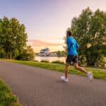 Un coureur en tenue bleue court sur une allée arborée en bord de Seine à Boulogne-Billancourt au coucher du soleil.