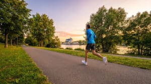 Un coureur en tenue bleue court sur une allée arborée en bord de Seine à Boulogne-Billancourt au coucher du soleil.