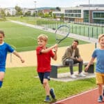 Enfants pratiquant diverses activités sportives dans un complexe moderne avec un éducateur en arrière-plan.