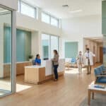 Hall d'accueil moderne et lumineux d'un centre médical avec réceptionniste, médecin et patient.