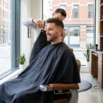 Un barbier professionnel coupe les cheveux d'un client souriant dans un salon moderne et lumineux à Boulogne-Billancourt.