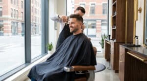 Un barbier professionnel coupe les cheveux d'un client souriant dans un salon moderne et lumineux à Boulogne-Billancourt.