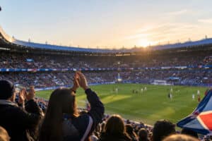 Spectateurs applaudissant dans les tribunes du Parc des Princes lors d'un match de football féminin au coucher du soleil.