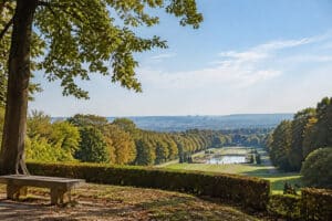Banc en pierre surplombant les jardins paysagers du parc de Saint-Cloud avec une vue sur Paris à l'horizon.